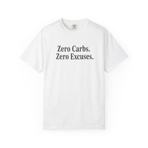 Puede incluir: Camiseta blanca con el texto negro "Zero Carbs. Zero Excuses." centrado en la parte delantera. La camiseta tiene cuello redondo y mangas cortas. La tela parece suave y cómoda.