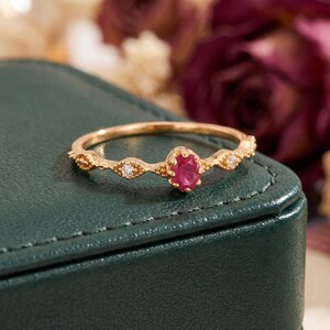 Peut inclure: Une bague en or ornée d'un rubis rouge central taille ovale, entouré de deux petites pierres claires taille ronde. L'anneau présente une texture perlée délicate et un design festonné, offrant une allure raffinée avec une finition polie.