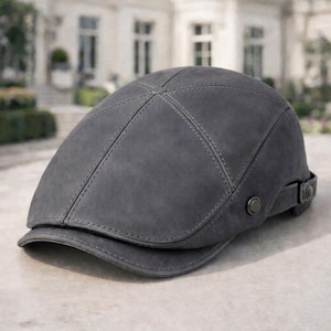 Puede incluir: Gorra plana gris con visera curva. Fabricada en material similar al ante, presenta costuras cosidas y una correa ajustable con hebilla metálica. Diseño clásico y atemporal.