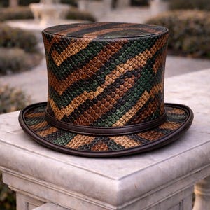 May include: A top hat with a snakeskin pattern in brown, green, and tan. It has a wide brim and a dark brown leather band. The hat is displayed on a stone surface. The hat's design is reminiscent of a reptile's skin.