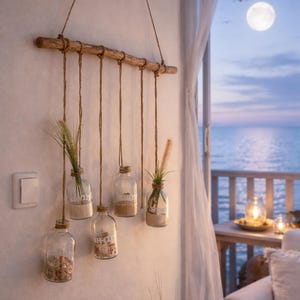 Può includere: Un'appendice da parete rustica con una trave di legno e sei bottiglie di vetro sospese con spago. Le bottiglie contengono sabbia, sassolini e vegetazione. Lo sfondo mostra una serena vista sul mare.