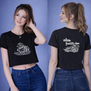 Puede incluir: Top corto negro con un gráfico de un lagarto con sombrero y chaleco. La parte trasera de la camiseta presenta un lagarto descansando bajo un letrero que dice "Nothing". La camiseta se combina con vaqueros azules.