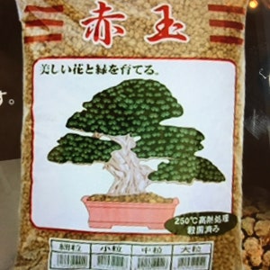 May include: A bag of Select Akadama bonsai soil, a type of Japanese clay soil, with the text "三赤玉三" and "美しい花と緑を育てる" in Japanese. The bag also features a drawing of a bonsai tree in a pink pot.