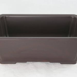 May include: A rectangular brown bonsai pot with a slightly raised rim and four small feet.