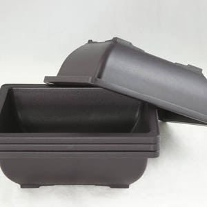 May include: A set of three brown plastic square plant pots. The pots are stacked on top of each other, with the top pot slightly offset to the side. The pots are made of a smooth, matte plastic.