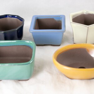 May include: Five ceramic bonsai pots in different colors and shapes. The pots are square, round, and hexagonal. The colors are blue, green, yellow, white, and dark blue.