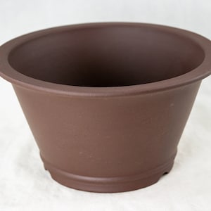 May include: A brown ceramic bonsai pot with a rounded top and a flared base. The pot has a smooth, matte finish.