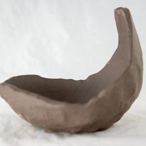 May include: A brown ceramic bowl with a unique, organic shape. The bowl is designed with a curved, crescent-shaped rim and a textured surface.