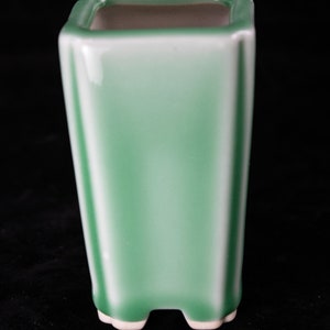 May include: A square green ceramic planter with a white glaze and four small feet.