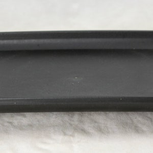 May include: A black plastic rectangular tray with four small feet. The tray is designed to hold a potted plant.