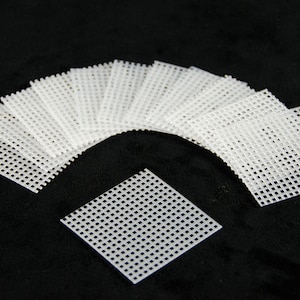 May include: A set of 15 white plastic mesh squares, arranged in a fan shape on a black background. The squares are approximately 2 inches by 2 inches.