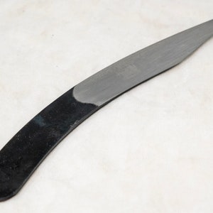 May include: A curved, black-handled knife with a silver blade. The blade is sharp and pointed.