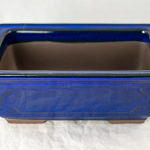 May include: A blue rectangular ceramic bonsai pot with a glazed finish. The pot has a slightly raised rim and a smooth, even surface.