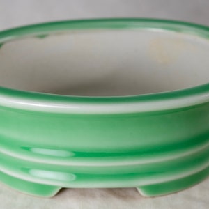 May include: A green ceramic oval planter with three white bands around the middle. The planter has a white rim and a smooth, glossy finish.