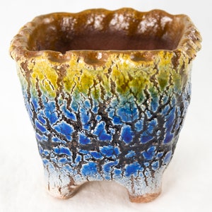 May include: A square ceramic planter with a blue, green, and yellow glaze. The planter has a textured surface and four legs.