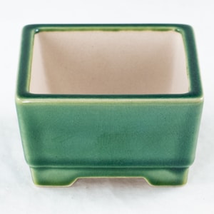 May include: A square green ceramic bonsai pot with a light brown interior and four small feet.