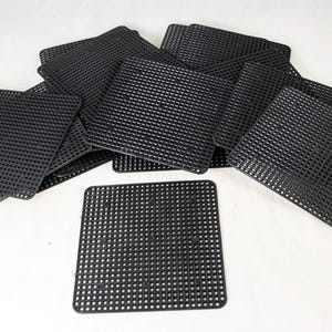 May include: A collection of black plastic canvas sheets, each with a square shape and a grid of evenly spaced holes. The sheets are scattered across a white surface, with some overlapping.