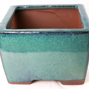 May include: Square ceramic planter with a green glaze. The planter has a slightly textured surface and a brown rim.