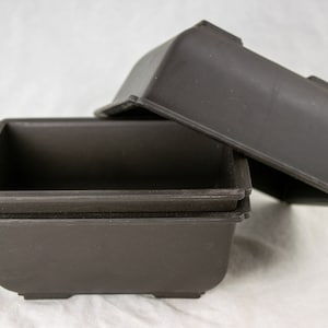 May include: Three brown plastic rectangular plant pots stacked on top of each other. The top pot is slightly tilted to the side.
