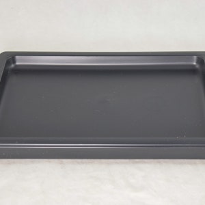 May include: A black plastic tray with a raised edge. The tray is rectangular and has a smooth surface.