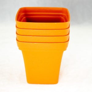 May include: A stack of four orange plastic square plant pots. The pots are stacked on top of each other, with the largest pot at the bottom and the smallest pot at the top.