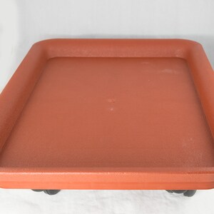 May include: A terracotta colored plastic plant tray with wheels. The tray is empty and ready to hold a potted plant.
