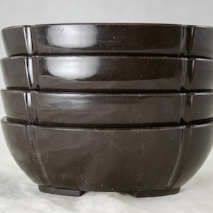 May include: A stack of four dark brown, glossy bowls. Each bowl has a unique, petal-like shape with a slightly flared rim and a small, rectangular foot. The bowls are stacked neatly on top of each other.