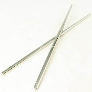 May include: A pair of silver chopsticks, crossed over each other, on a white background.