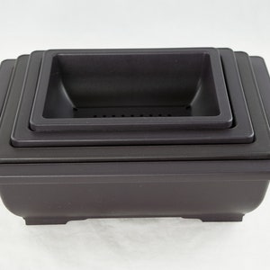 May include: Set of four black square plastic bonsai pots, stacked in decreasing size. The largest pot has a drainage hole and a lip around the top edge.