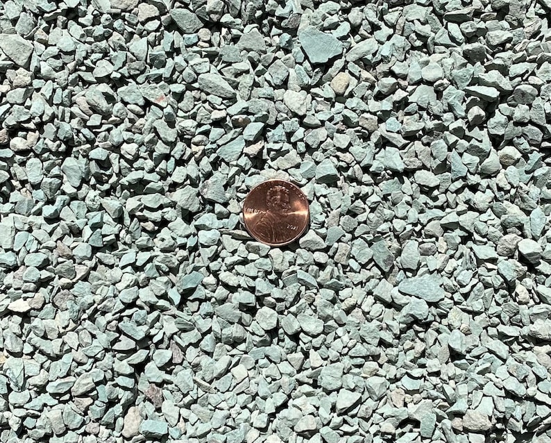 K&ouml;nnte beinhalten: Nahaufnahme von gr&uuml;nem Erbsenkies, mit einem Penny als Gr&ouml;&szlig;envergleich. Der Kies ist klein und gleichm&auml;&szlig;ig in der Gr&ouml;&szlig;e.