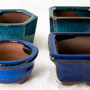 May include: Four ceramic bonsai pots in different shapes and sizes. Two are square, one is hexagonal, and one is round. The square pots are blue and green glazed, while the round and hexagonal pots are blue glazed.