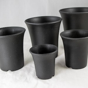 May include: A collection of five black, tapered plant pots of varying sizes. The pots have a matte finish and a slightly flared rim. The pots are designed for indoor or outdoor use and are made of a durable material.