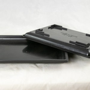 May include: Two black plastic trays, one stacked on top of the other. The top tray has a raised edge and the text "MADE IN CHINA" printed on the bottom.