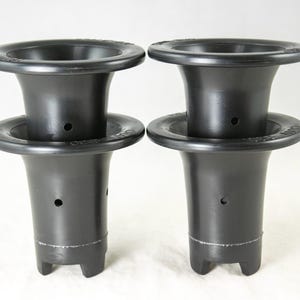 May include: Two black plastic funnels with a wide top and a flared body. Each funnel has a circular base and a small hole in the side. The funnels are designed with a three-pronged base for stability.