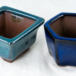 May include: Two ceramic bonsai pots, one square and teal green, the other hexagonal and dark blue.