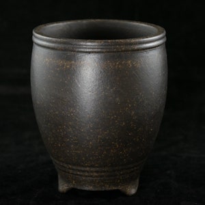 May include: A dark brown ceramic pot with a rounded body and three small feet. The pot has a rough, textured surface.