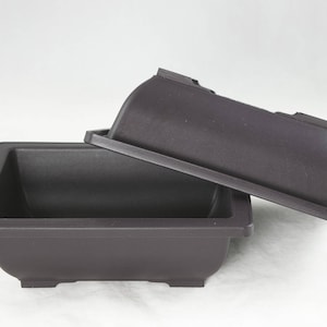 May include: Two black plastic rectangular bonsai pots, one stacked on top of the other. The top pot is slightly smaller than the bottom pot.