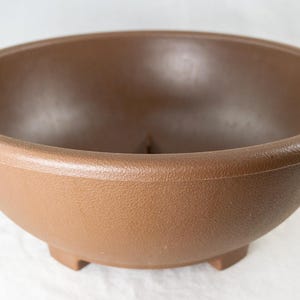 May include: A brown ceramic bonsai pot with a textured surface and a drainage hole in the bottom.