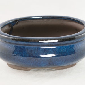May include: A blue oval ceramic bonsai pot with a dark blue rim and a slightly textured surface.