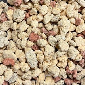 May include: Close-up of a pile of small, irregularly shaped rocks. The rocks are primarily beige and off-white, with some reddish-brown stones interspersed throughout. The texture appears porous and rough, suggesting a natural material.