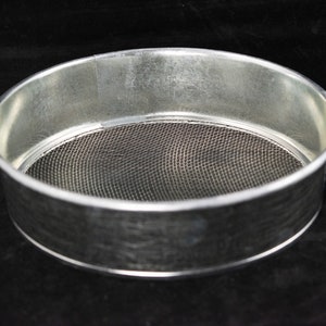 May include: A silver metal sieve with a mesh bottom. The sieve is round and has a diameter of about 10 inches.