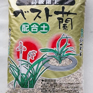 May include: A bag of orchid potting soil with Japanese text and illustrations of orchids. The bag is clear, allowing the soil to be visible. The soil appears to be a light beige color. The bag has a green and gold label with Japanese text and illustrations.