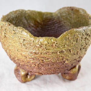 May include: A small, green and brown ceramic pot with a textured surface and three legs.