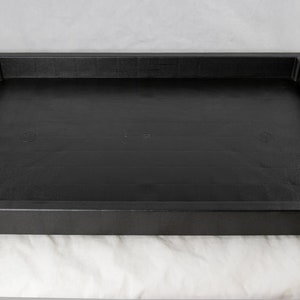 May include: A black plastic tray with a raised edge. The tray is rectangular and has a smooth surface.