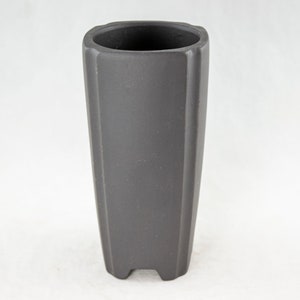 May include: A dark gray ceramic planter with a square top and a rounded bottom. The planter has a textured surface and four small feet.