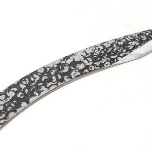 May include: A silver knife with a black patterned blade. The blade is curved and has a pointed tip.