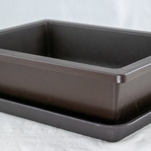 May include: A brown plastic rectangular planter with a matching brown plastic tray. The planter is designed to hold a plant and the tray catches excess water.