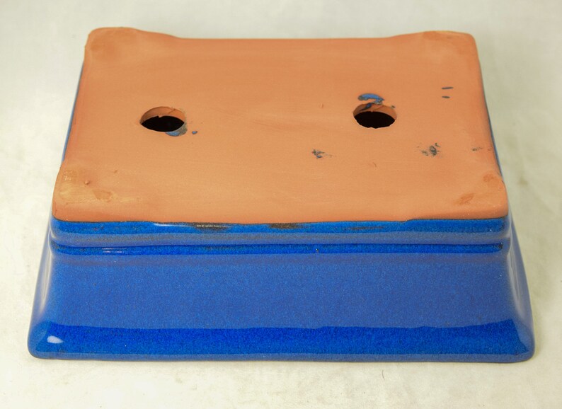 May include: A blue glazed rectangular ceramic planter with two drainage holes in the bottom. The planter is made of terracotta and has a blue glaze on the outside.