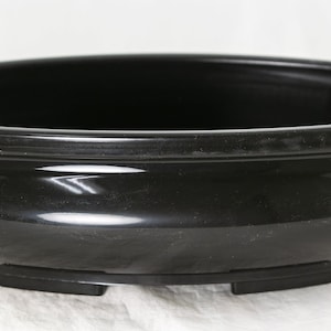 May include: A black oval ceramic bonsai pot with a glossy finish and three small feet.