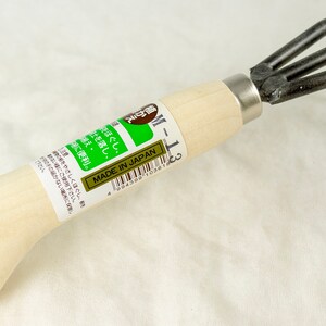 May include: A wooden handled gardening tool with four metal prongs. The tool is labeled "M-1-3" and "Made in Japan".